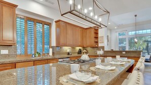 A modern kitchen with granite countertops, wooden cabinets, and a large island with dining setup.