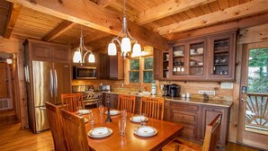 Interno di una baita in legno con un tavolo da pranzo per quattro persone, una cucina con pensili in legno, un frigorifero e un forno a microonde.