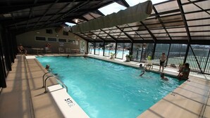 An indoor swimming pool with clear water, a covered roof, and a view of the outside. - Branson Condo at Pointe Royale with Indoor Pool and Hot Tub walking distance to (Branson)