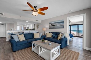 A living room with a ceiling fan, a dining area, and a view of the ocean.