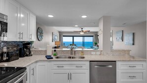 Una cocina moderna con armarios blancos, un lavavajillas de acero inoxidable y un amplio ventanal con vista al océano.