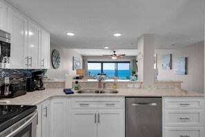 A modern kitchen with white cabinets, a stainless steel dishwasher, and a view of the ocean.