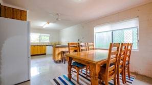 Une cuisine avec des meubles de rangement en bois, une table à manger avec des chaises et un réfrigérateur.