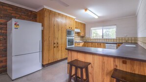 A kitchen with wooden cabinets, a white refrigerator, an oven, and a window. - Croydon Ave 50 - Currimundi (CURRIMUNDI)