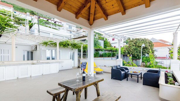 A covered outdoor patio with a wooden table, benches, and seating. - Miracle Apartments (Dubrovnik)
