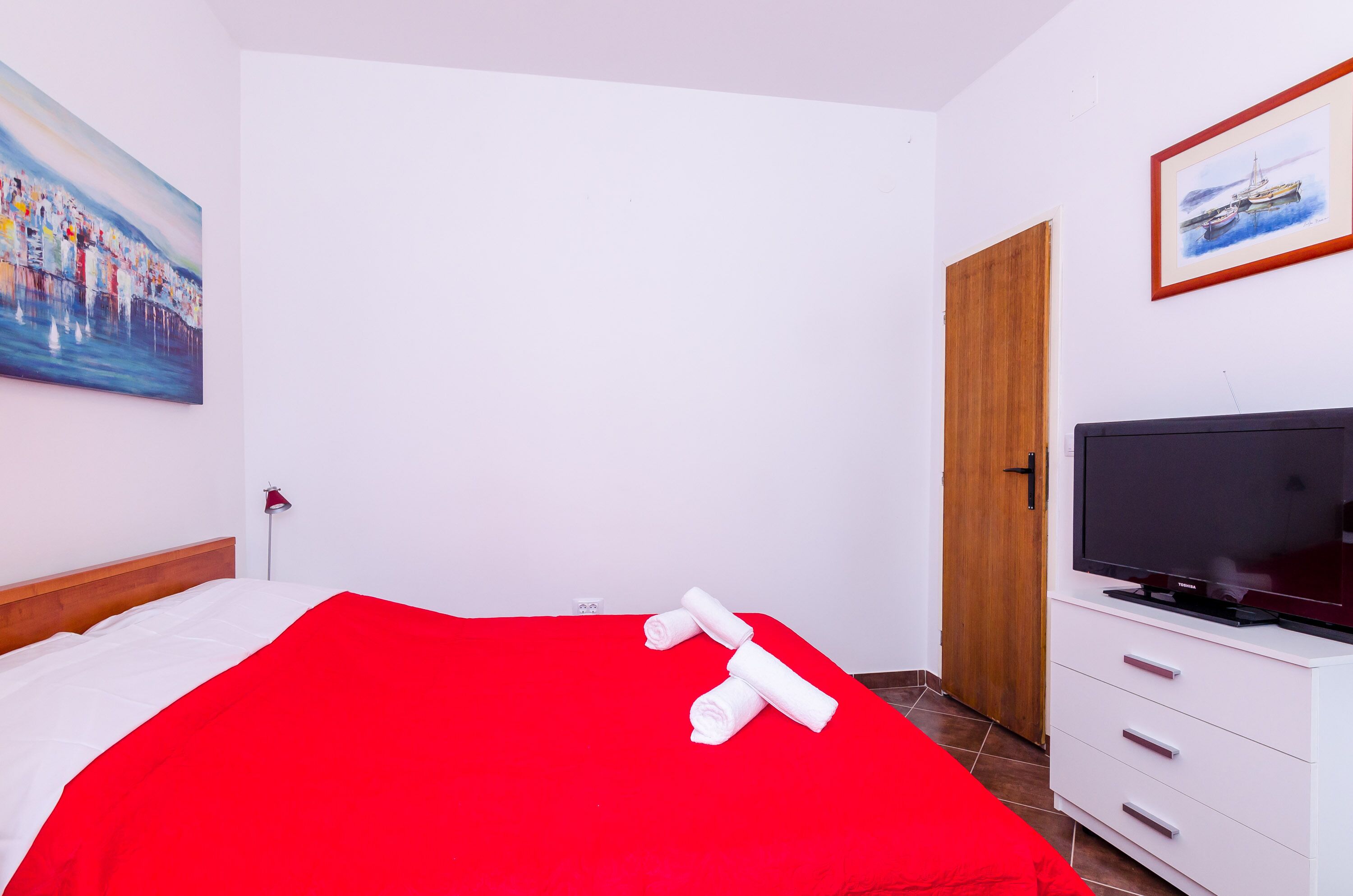 Een hotelkamer met een bed, een televisie, een houten deur en een schilderij aan de muur.
