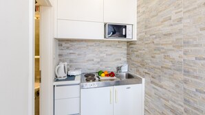 A compact kitchenette with a microwave, stove, sink, and white cabinets. - Miracle Apartments (Dubrovnik)