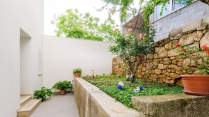 A narrow courtyard with a stone wall, potted plants, and a small tree with pink flowers. - Miracle Apartments (Dubrovnik)