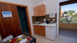 A small kitchenette with a wooden cabinet, a coffee maker, and a dishwasher. There is a dining table with plates and a vase of flowers. - John Apartments First Floor (Corfu)