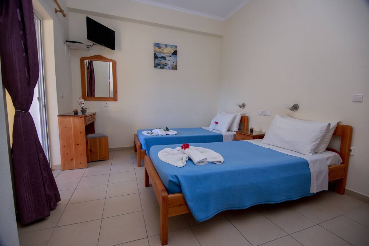 A hotel room with two beds, a wooden dresser, a television mounted on the wall, and a painting.