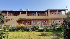 A two-story building with a balcony, a staircase, and a garden in front. - John Apartments First Floor (Corfu)