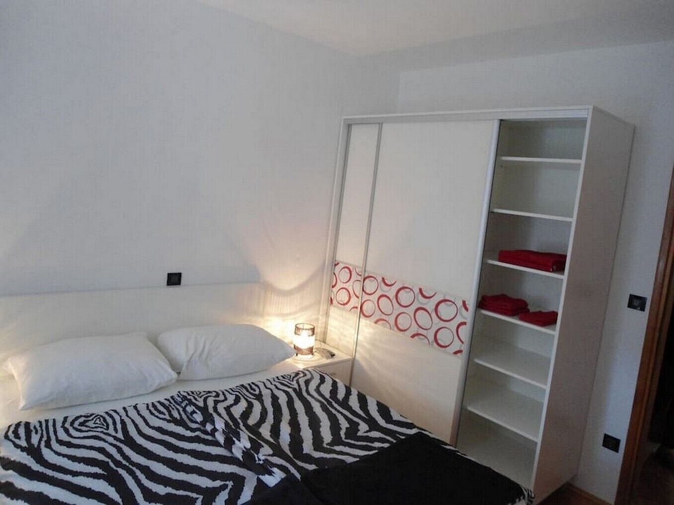 A bedroom with a bed, a bedside table with a lamp, and a wardrobe with shelves.