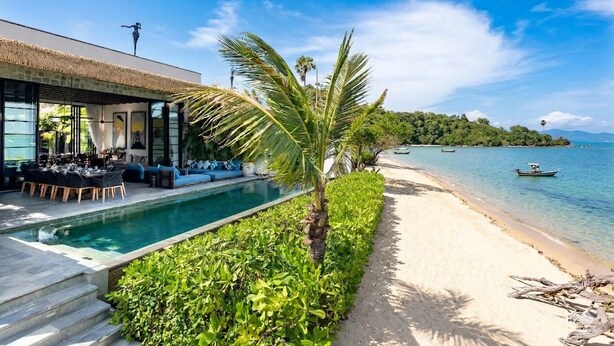 A poolside area with a dining setup, a beach, and boats in the water. - Clay Beach Samui (Koh Samui)