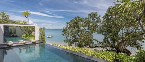A modern infinity pool with clear water, surrounded by lush greenery and overlooking a calm sea.