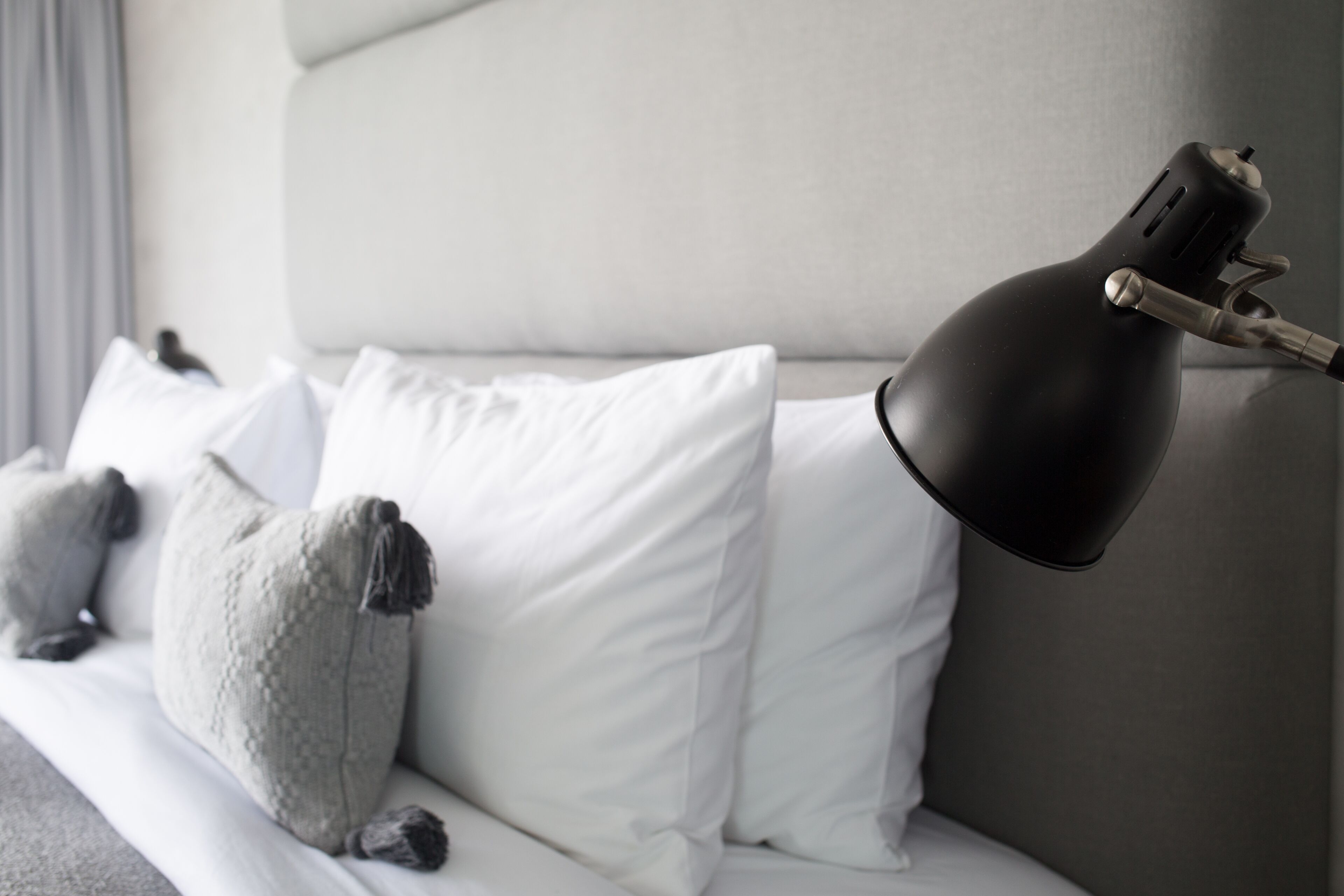 A bed with white and gray pillows, a black desk lamp, and a grey headboard.