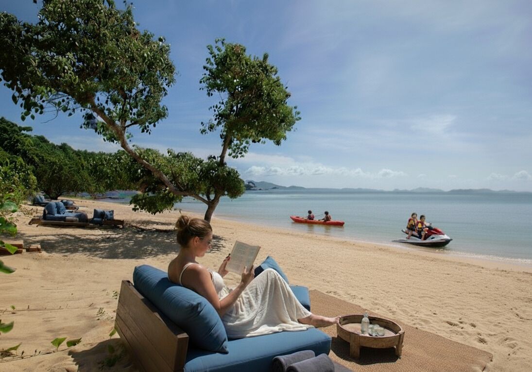 Una spiaggia con una donna che legge su un divano blu, un albero e un kayak nell'acqua.