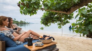 A beach setting with a wooden table under a tree, a blue sofa, and a view of the sea. - Clay Beach Samui (Koh Samui)