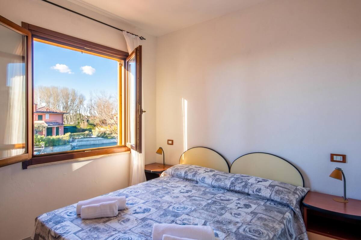 Une chambre à coucher avec un lit, une table de chevet, une lampe et une fenêtre avec des rideaux.