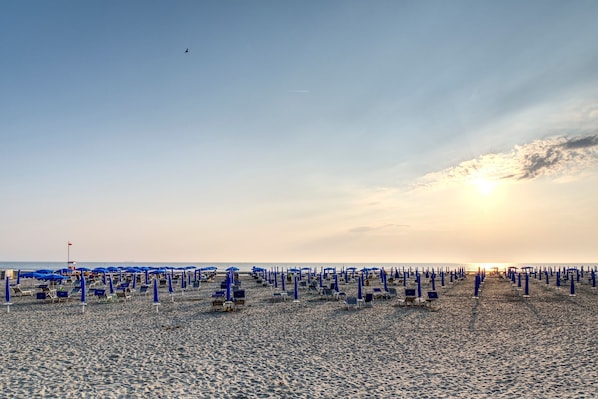 Een strand met rijen blauwe parasols en ligstoelen.