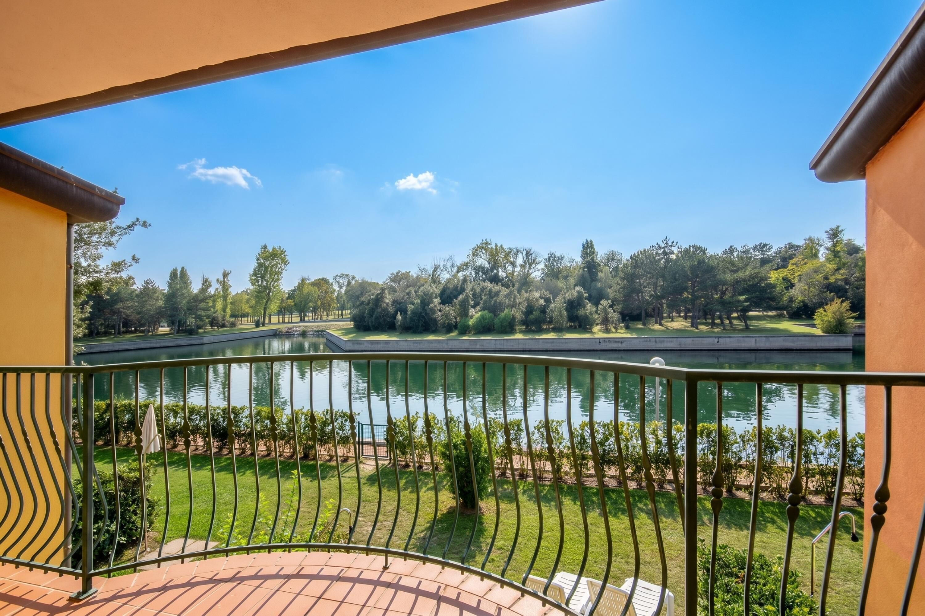 A balcony with a view of a lake, greenery, and a bridge.