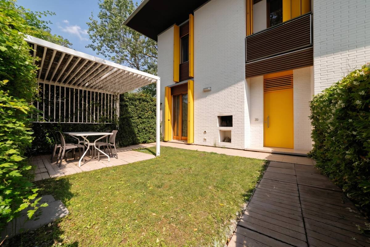 Une maison moderne dotée d’un patio couvert, d’un petit jardin et d’une terrasse en bois.