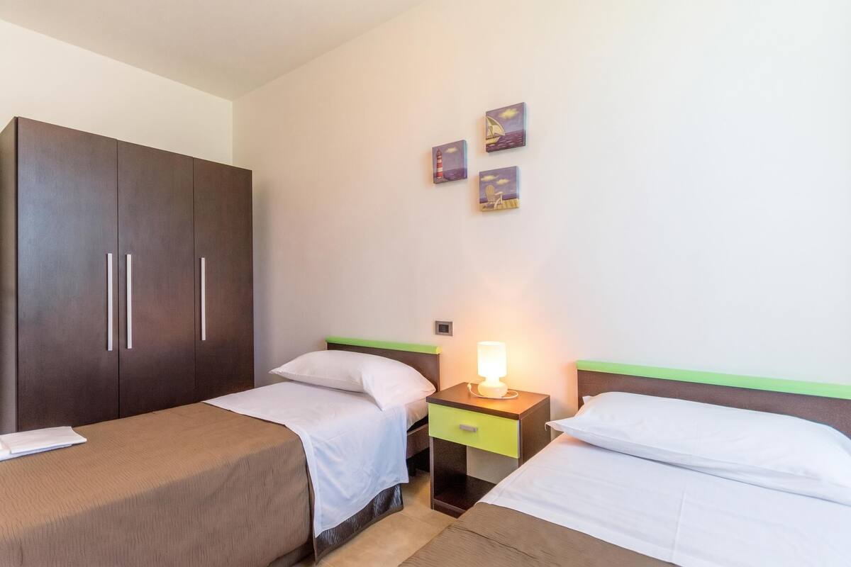 Une chambre d’hôtel avec deux lits, une armoire, une table de chevet avec une lampe et trois œuvres d’art mural.