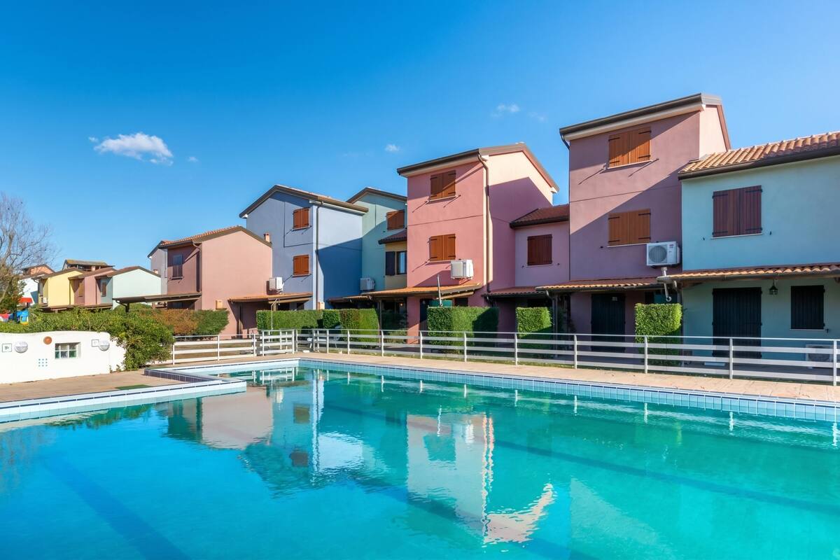 Une piscine entourée d’une clôture blanche, elle-même bordée de bâtiments colorés dotés de balcons.