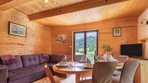 A wooden cabin interior with a sofa, dining table, chairs, and a TV. - Krasevec Lodge With Garden & Pool (Bloke)