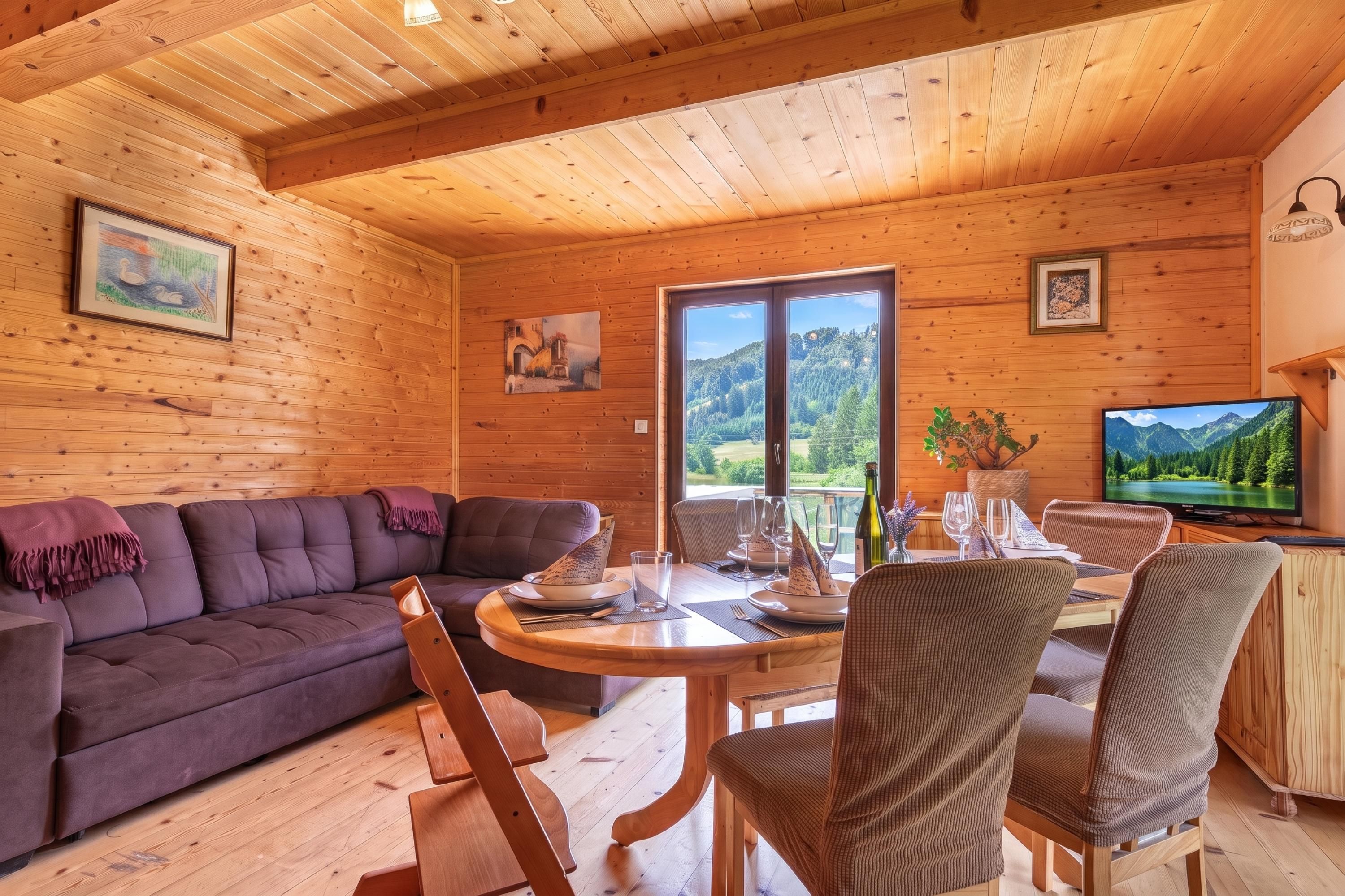 A wooden interior with a sofa, dining table, chairs, and a television.