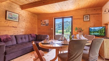 A wooden interior with a sofa, dining table, chairs, and a television.
