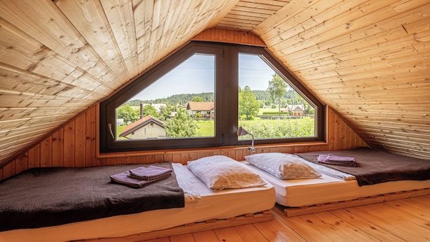 A cozy attic bedroom with two beds, wooden walls, and a large window offering a view of the countryside. - Krasevec Lodge With Garden & Pool (Bloke)