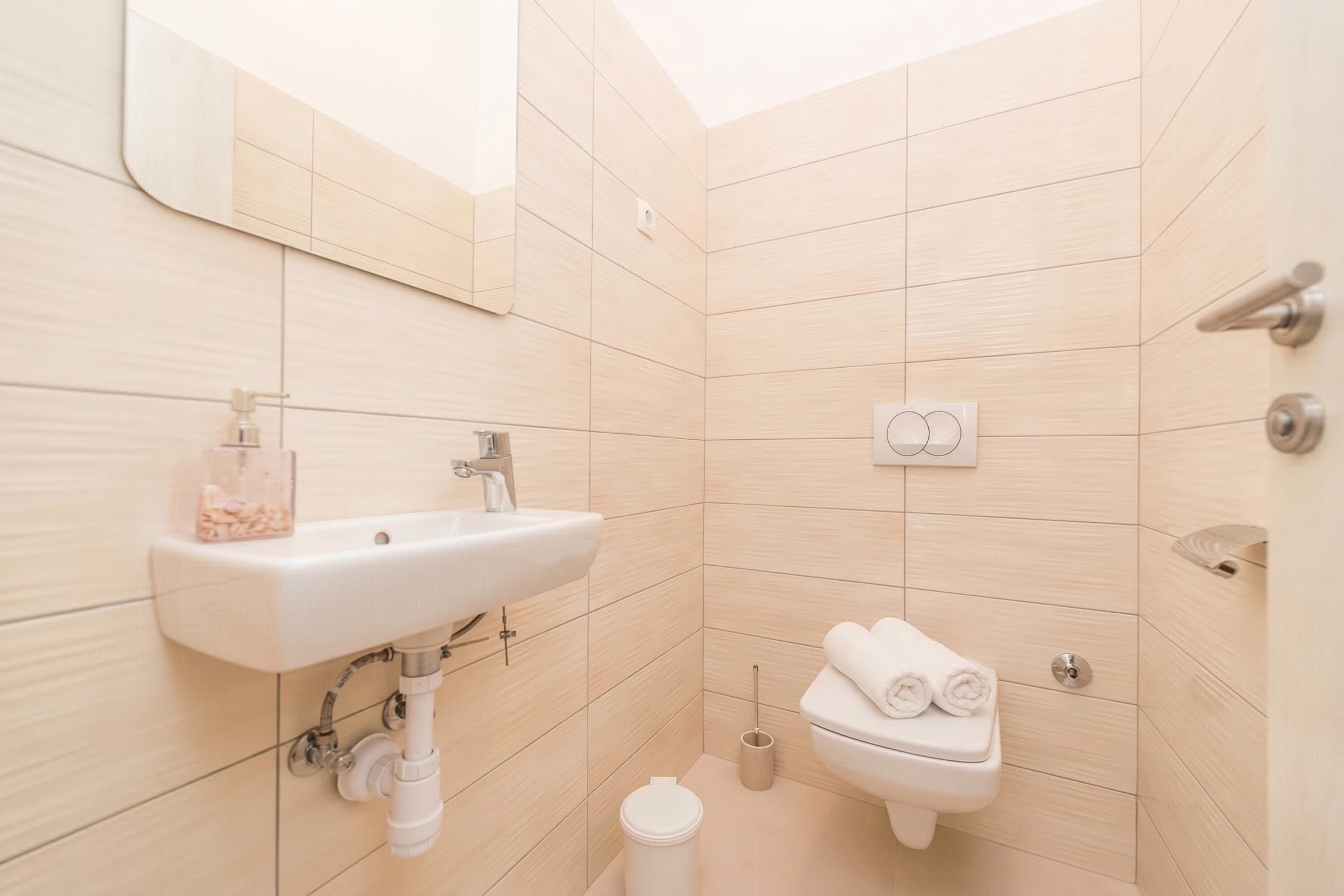 Et badeværelse med en hvid vask, spejl, toilet og håndklædestang.