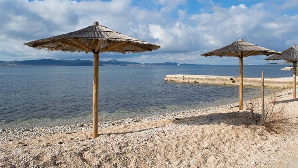 A beach with thatched umbrellas and a pebbly shore. - Family Friendly Pool House Ana Near Zadar (Bibinje)