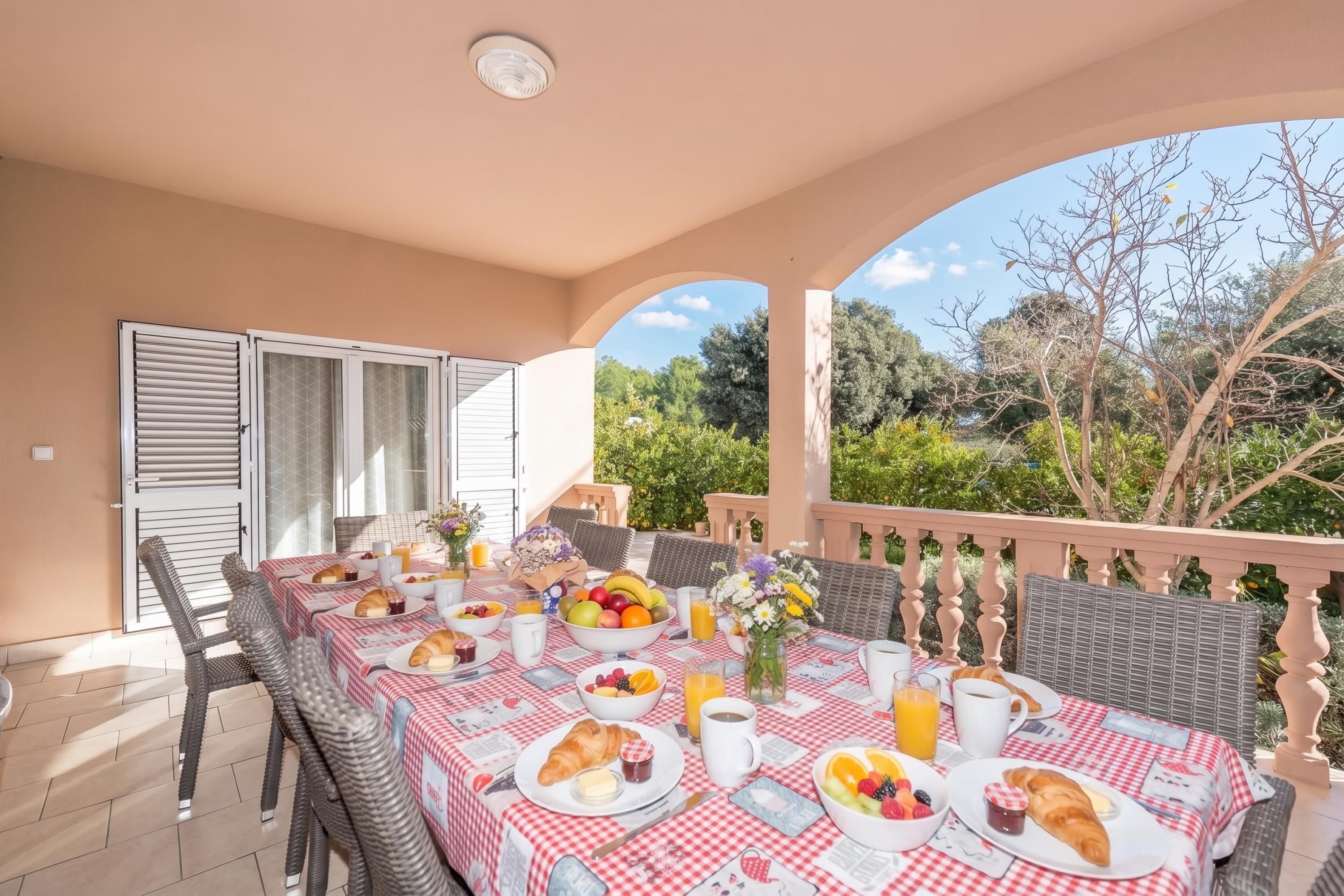 An outdoor dining area with a checkered tablecloth, wicker chairs, and a view of the surrounding greenery.