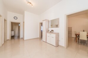 A spacious room with a wooden cabinet, a dining area with chairs, and a large mirror on the wall.