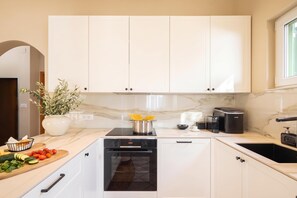 A modern kitchen with white cabinets, a black dishwasher, and a marble countertop.