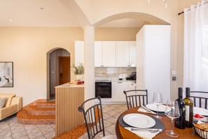 A modern kitchen with white cabinets, a dining area with a round table, and a staircase leading to an upper level.