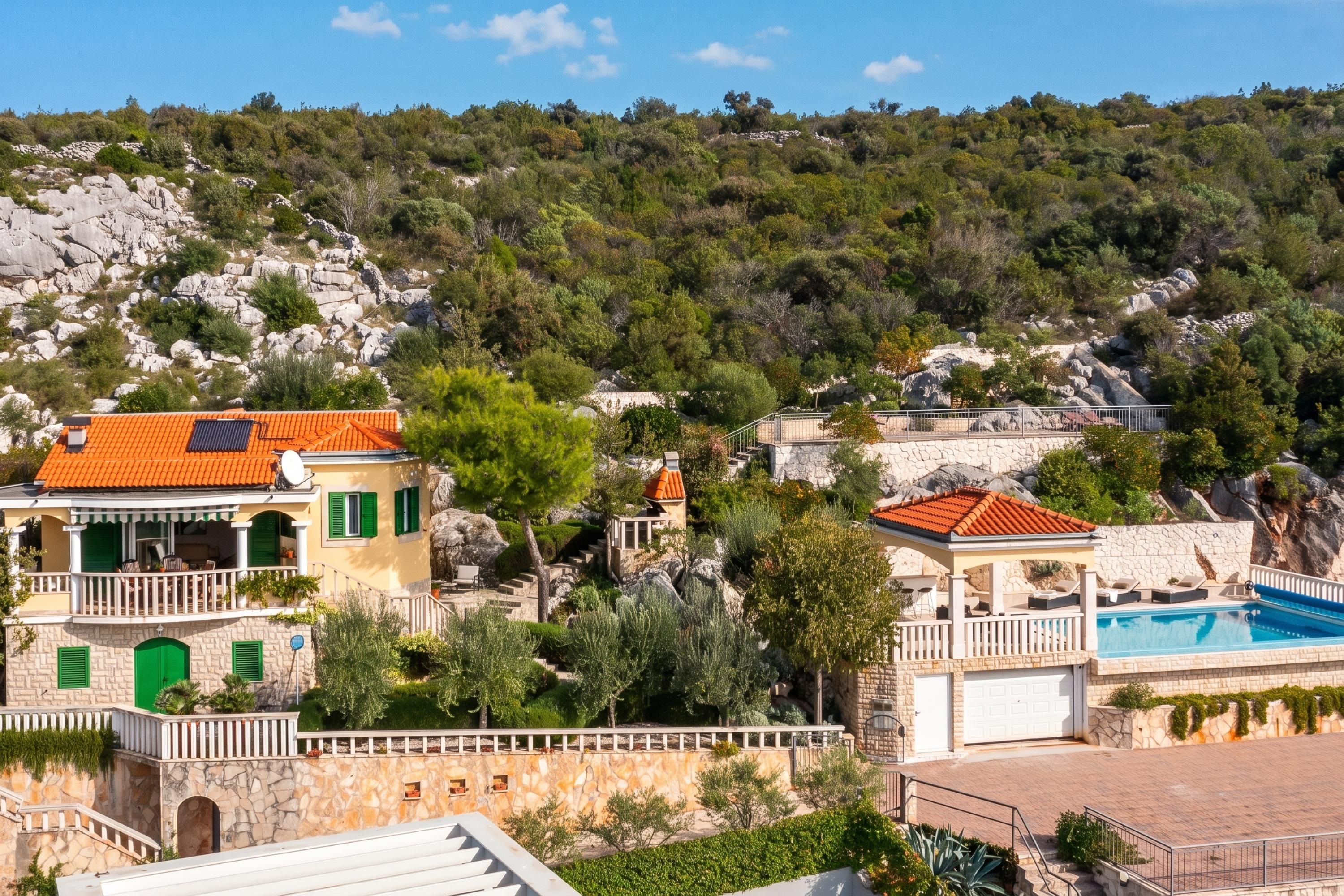A coastal property with a swimming pool, stone walls, and a hillside view.