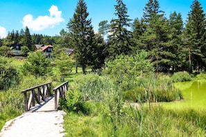 A wooden bridge leading to a pond surrounded by dense trees and houses in the background. - House Fortin With Sauna Near Bloke Lake (Bloke)