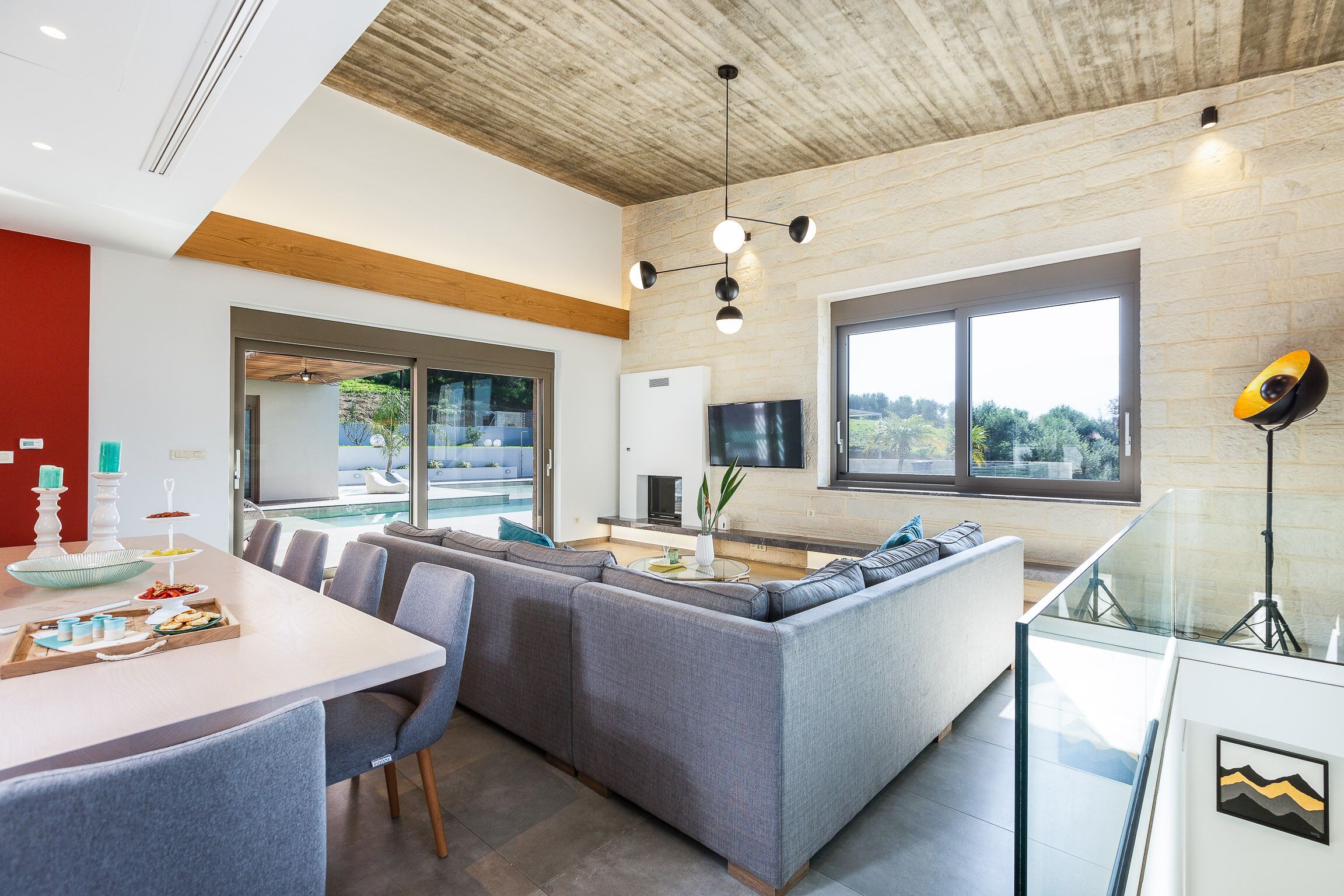 Uma sala de estar moderna com uma mesa de jantar, sofás cinzas, uma TV e uma janela grande com vista para o exterior.