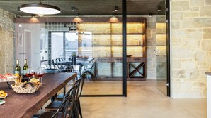 A modern dining area with a long wooden table, chairs, and a basket of bread and wine bottles. - Villa Aori (Apokoronas)