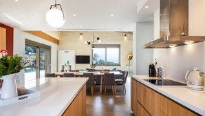 A modern kitchen with a central island, wooden cabinets, and a large window providing natural light. - Villa Aori (Apokoronas)
