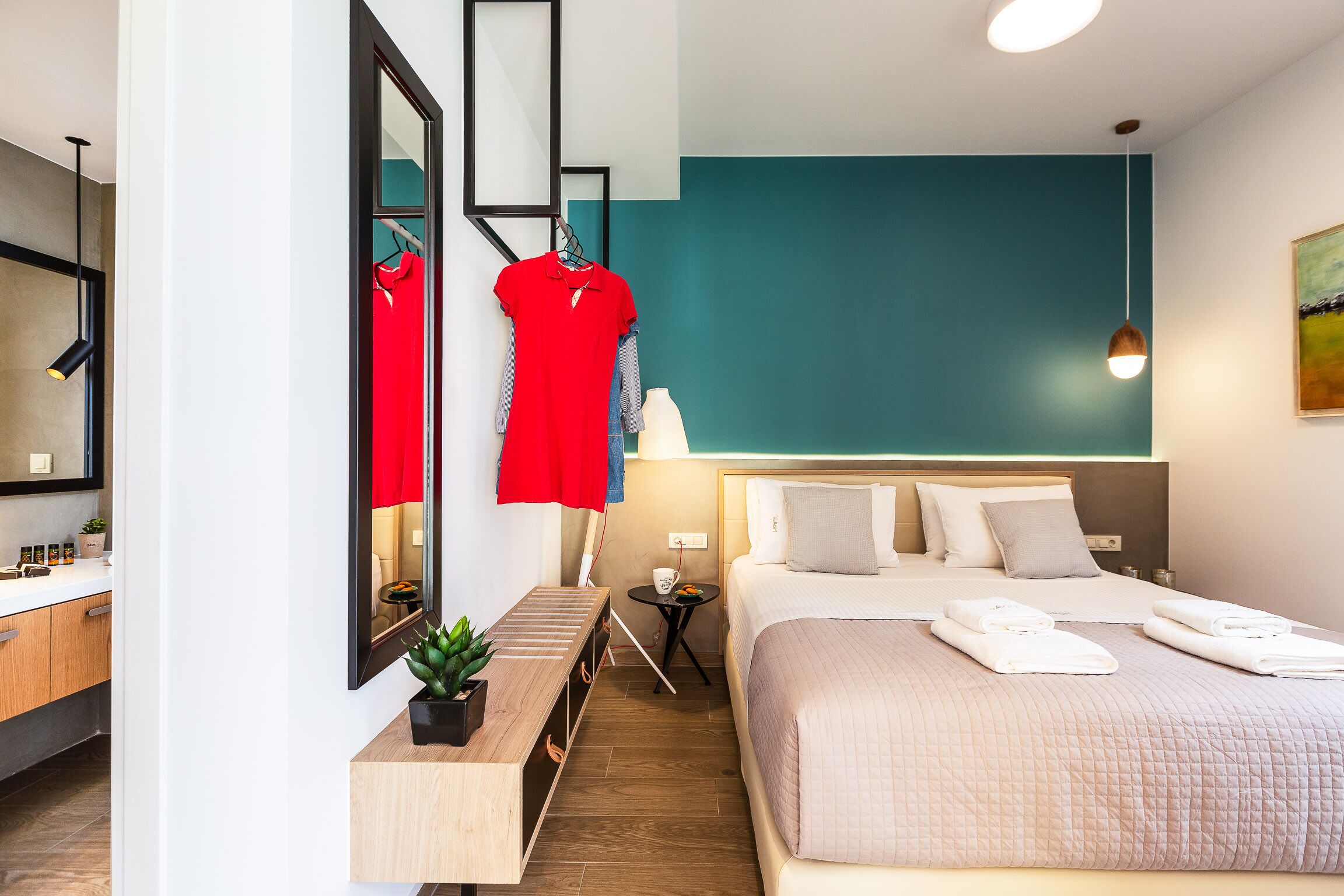 Et moderne hotelværelse med seng, sengebord, spejl og et lille bord med en plante.