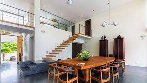 Un comedor amplio con una gran mesa y sillas de madera, una escalera y vistas al verdor exterior.