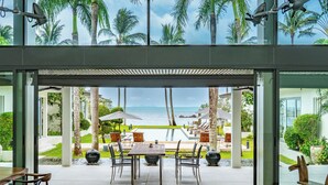 Un área de comedor al aire libre moderna con vistas al océano, palmeras y una piscina.
