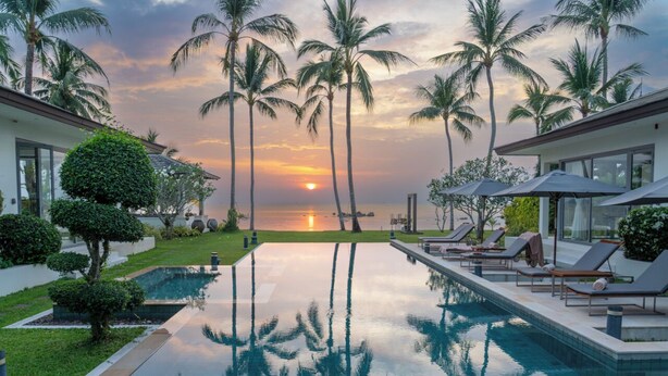 Una piscina con palmeras, un atardecer y sillas de descanso.