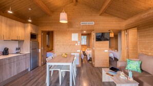 Una cabaña de troncos moderna con interior de madera, un comedor y una sala de estar con sofá y televisor.