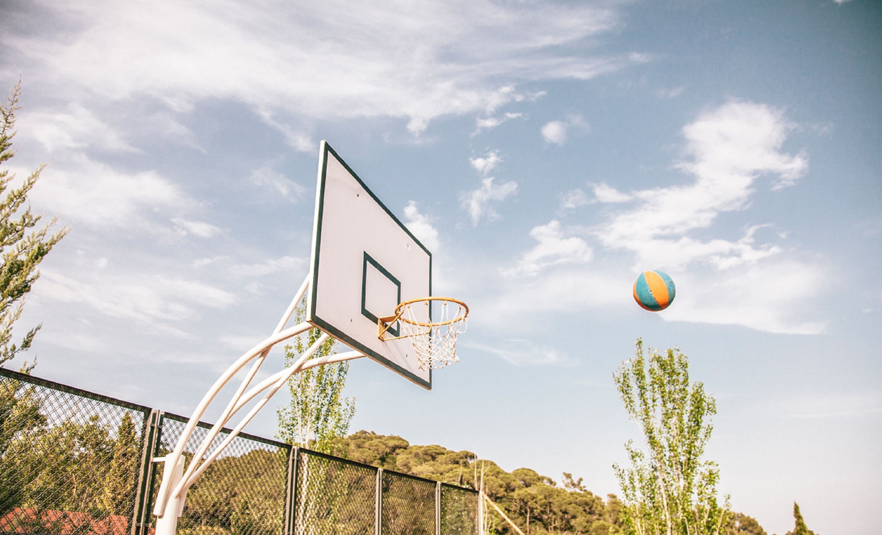 A basketball hoop with a net, a clear sky, and a volleyball in mid-air.