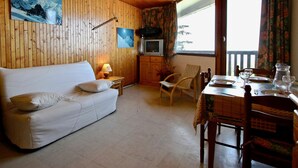 A wooden cabin interior with a white sofa, a dining table set for two, and a television in the corner. - Cozy studio at the slopes with balcony, pets welcome (Chamrousse)