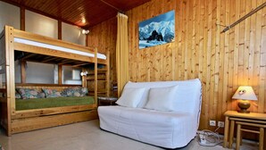 A wooden cabin interior with a bunk bed, a white sofa, a small table with a lamp, and a painting of a mountain on the wall. - Cozy studio at the slopes with balcony, pets welcome (Chamrousse)